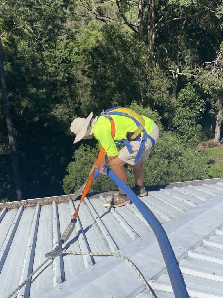 Man on roof cleaning gutters in Brisbane. Wearing hi vis yellow and a hat.